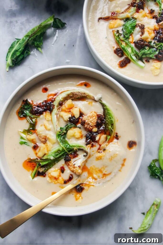 Roasted cauliflower cheese soup in 2 bowls on a grey marble background.
