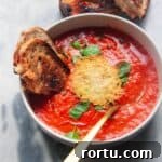 Roasted red pepper and tomato soup in a white bowl with grilled cheese dipped in.