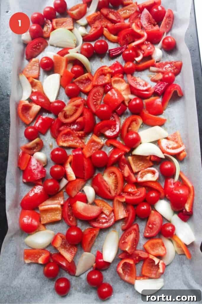 Sliced tomatoes, bell peppers, garlic and onion on a baking sheet.