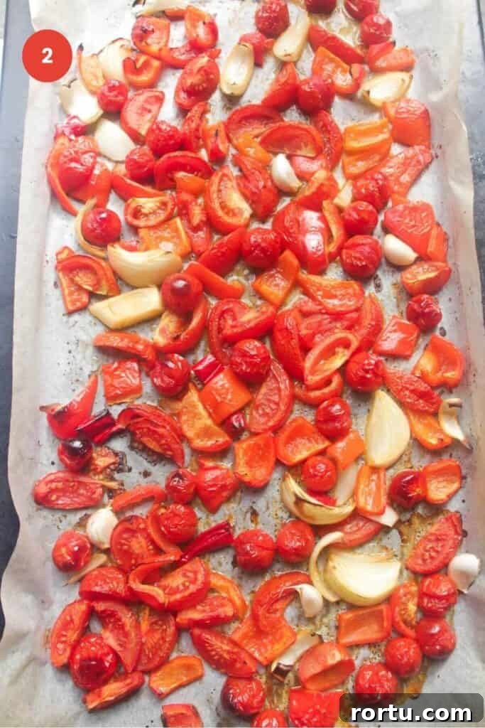 Roasted tomatoes, bell peppers, garlic and onion on a baking sheet.
