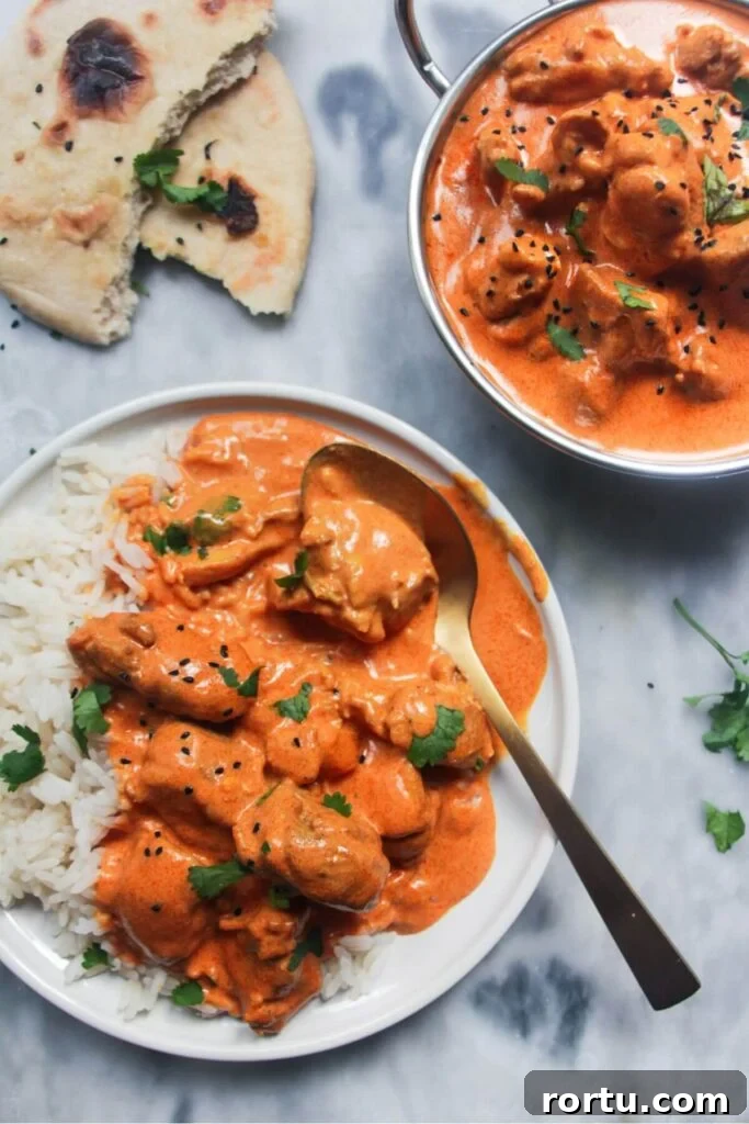 White plate with rice and butter chicken with bowl of butter chicken in the background and garlic naan.