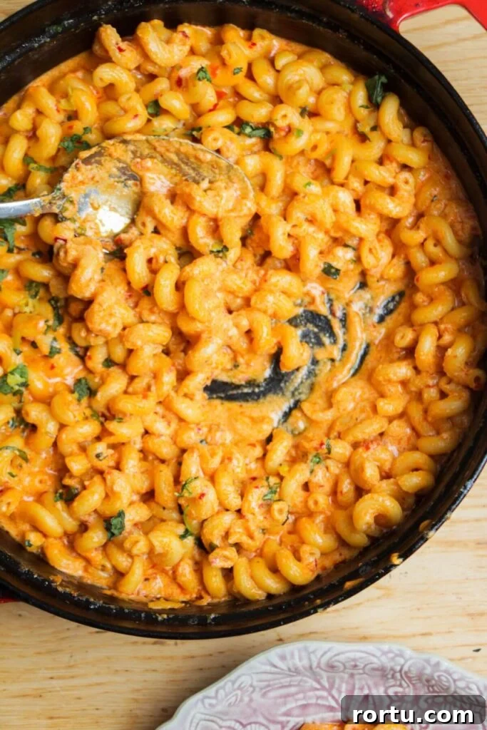 Spicy mac and cheese in a large black skillet with a silver spoon inside.
