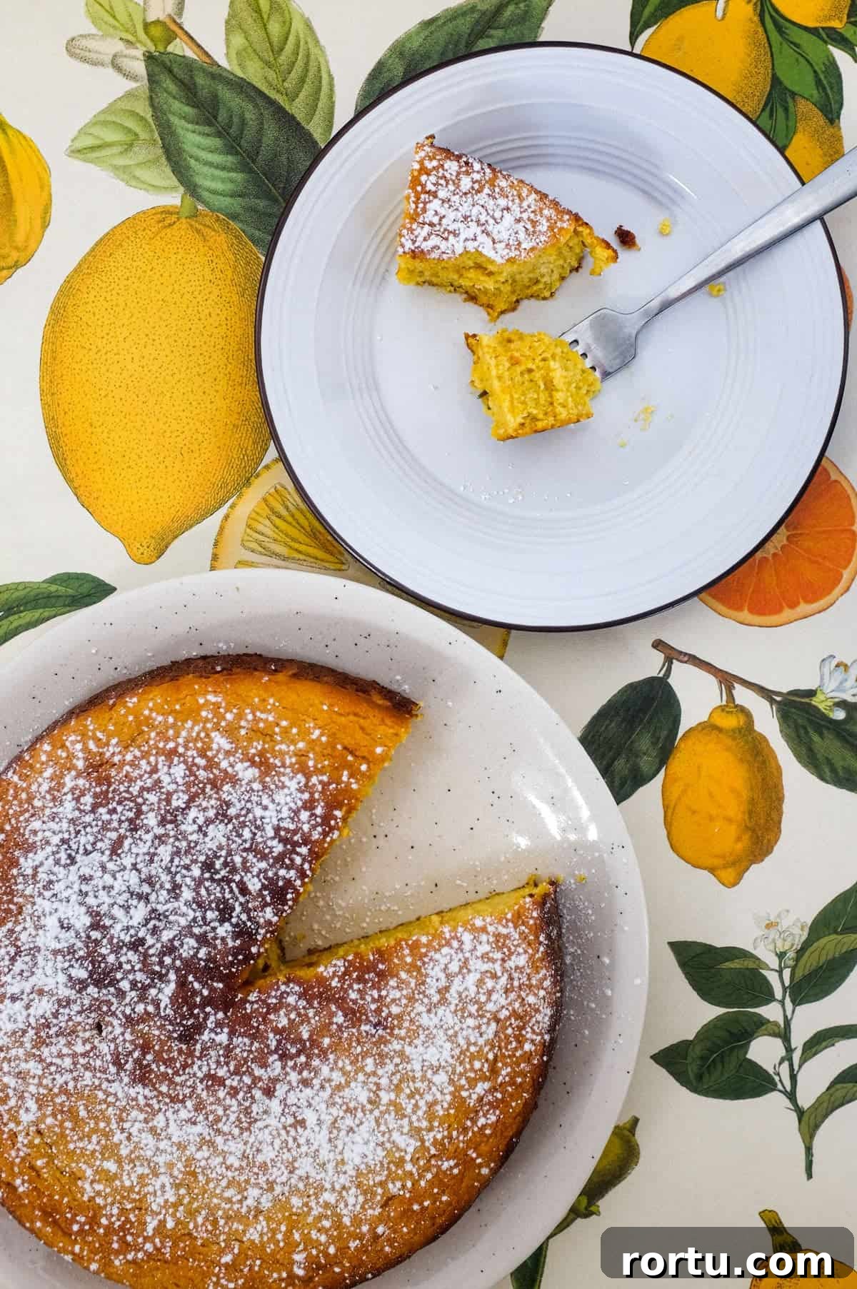 A flourless orange cake and slice of cake sit on plates on a colourful background of citrus fruit illustrations.