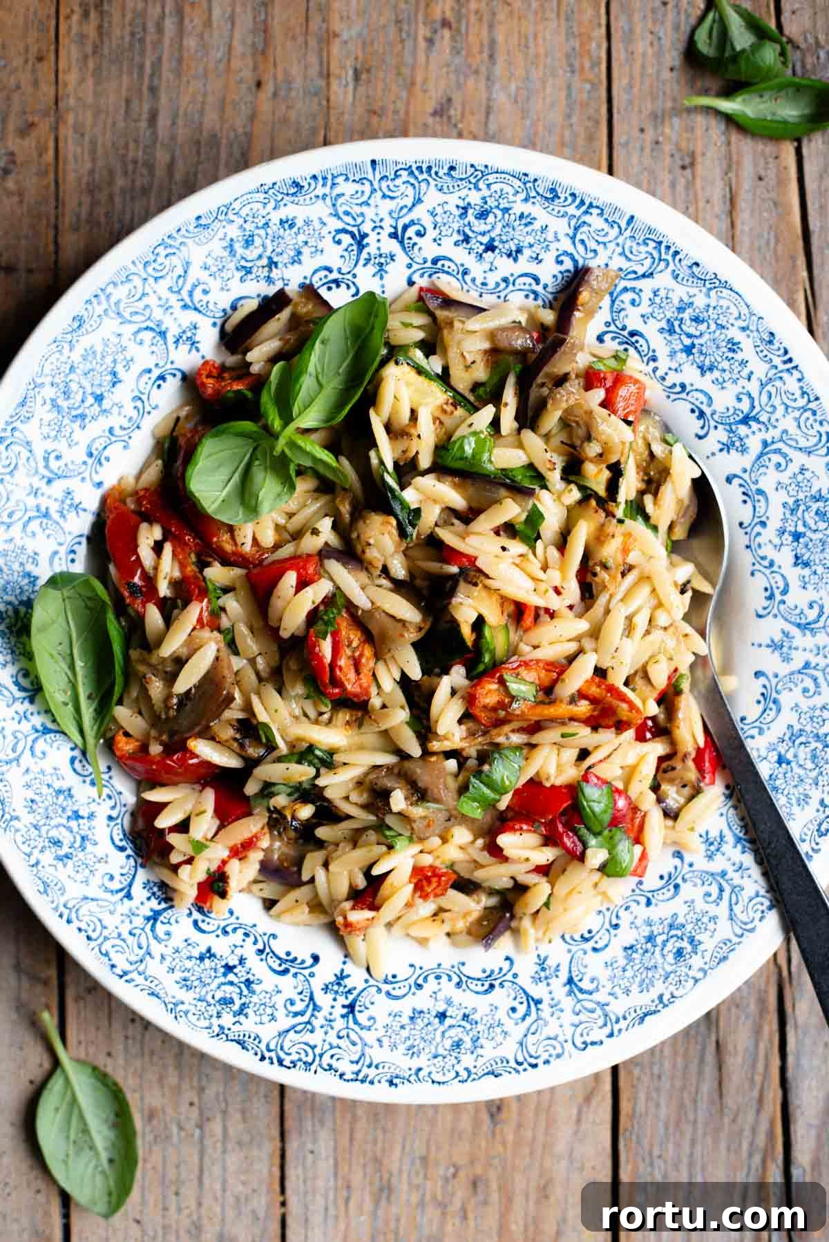 Grilled Summer Vegetables Orzo Salad with Lemon Herb Dressing 2 An orzo pasta salad with grilled veg in a blue bowl with a serving spoon at the side. The background is rustic wood.