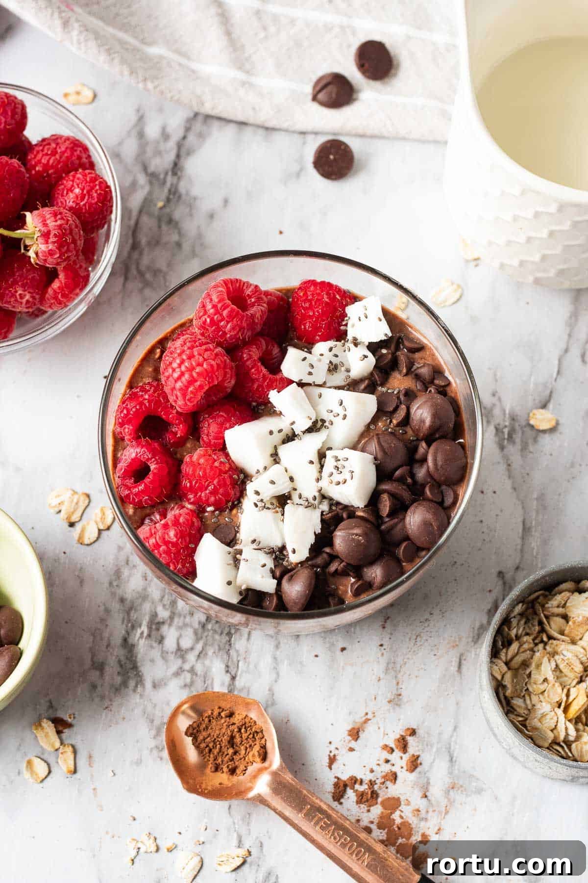 Brownie Batter Overnight Oats with spoonful of cocoa powder and bowl of raspberries nearby.