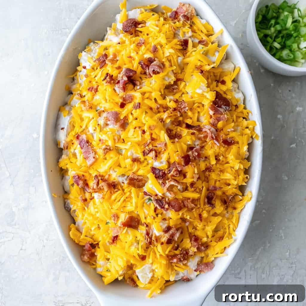 Twice Baked Potato Casserole topped with shredded cheddar and crumbled bacon, ready for the oven.