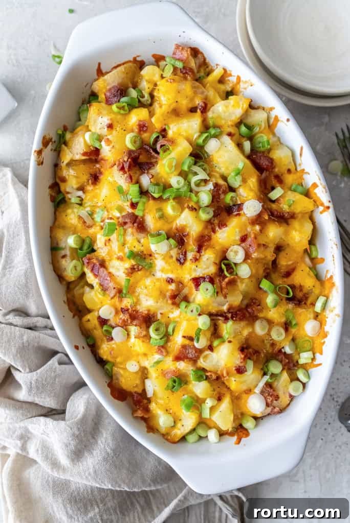 wice Baked Potato Casserole in a white baking dish topped with melted cheddar, crisp bacon, and green onions, set on a neutral linen with forks and plates nearby.