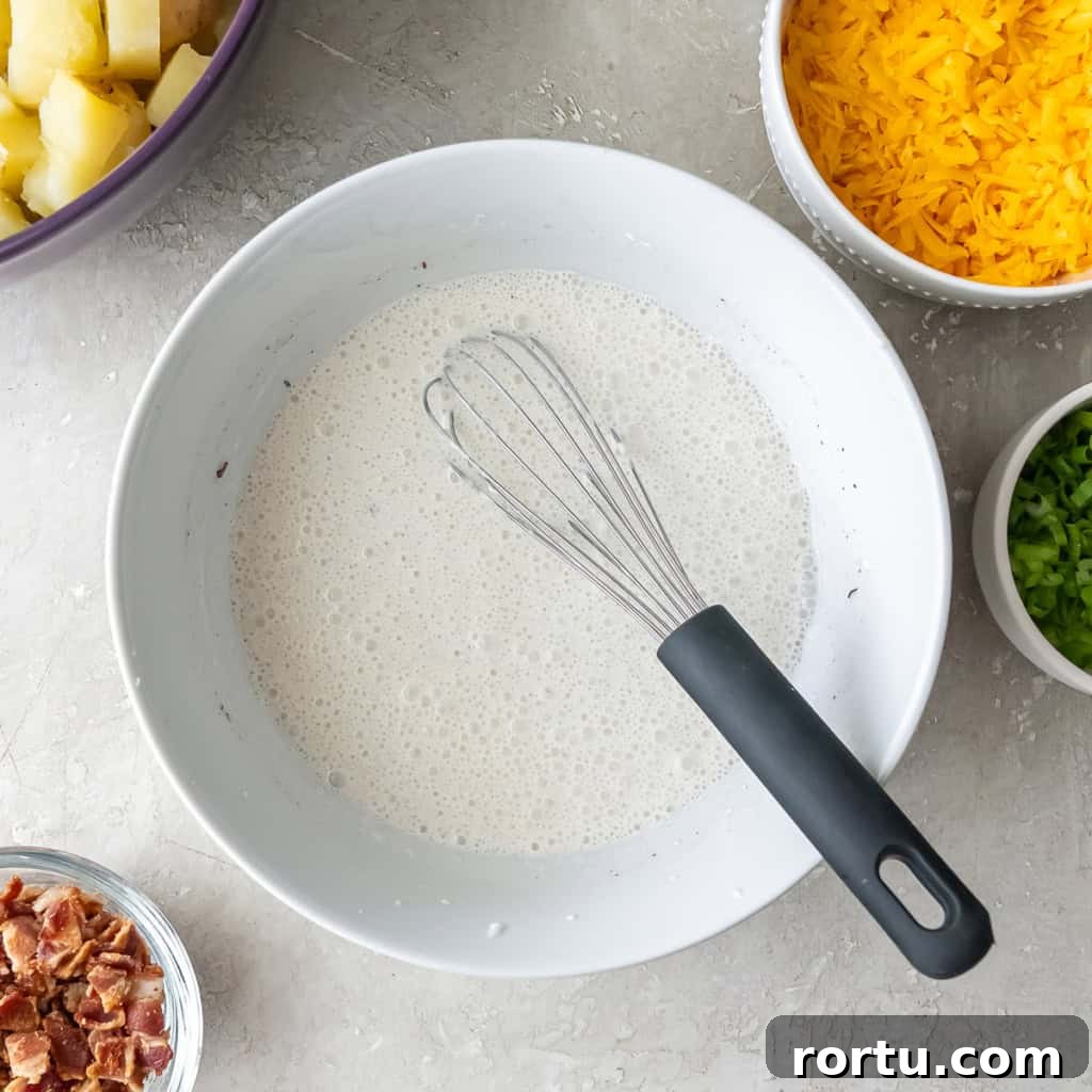 A whisk resting in a bowl filled with a sour cream mixture.