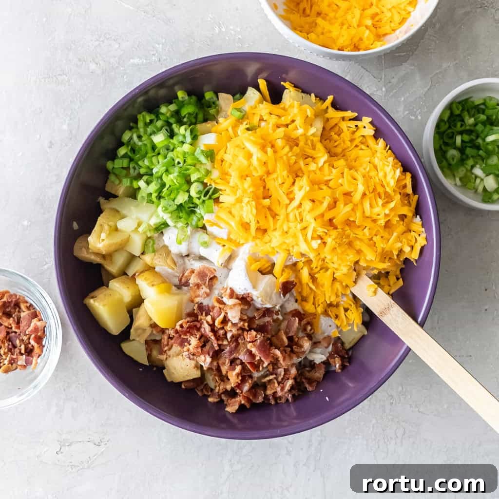 Chopped potatoes topped with shredded cheddar, green onions, and crumbled bacon before mixing.