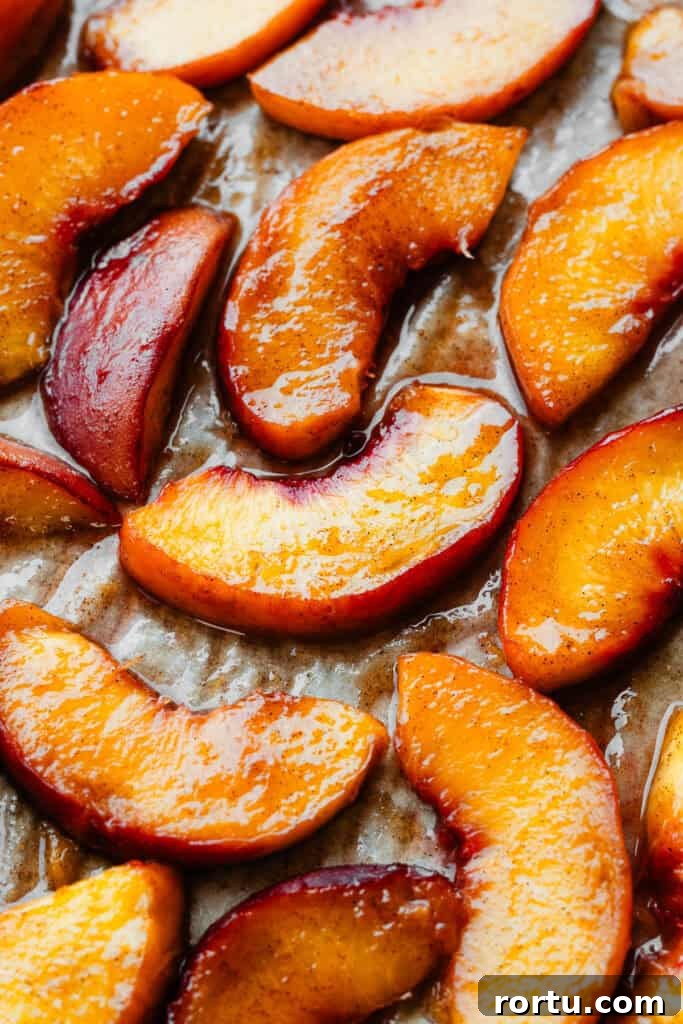 A close-up of juicy roasted peach slices on a parchment paper lined baking sheet.