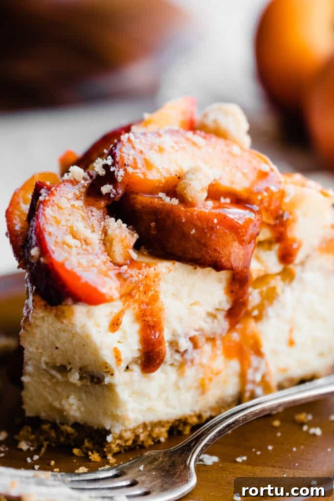 A slice of peach cobbler cheesecake topped with roasted peaches.