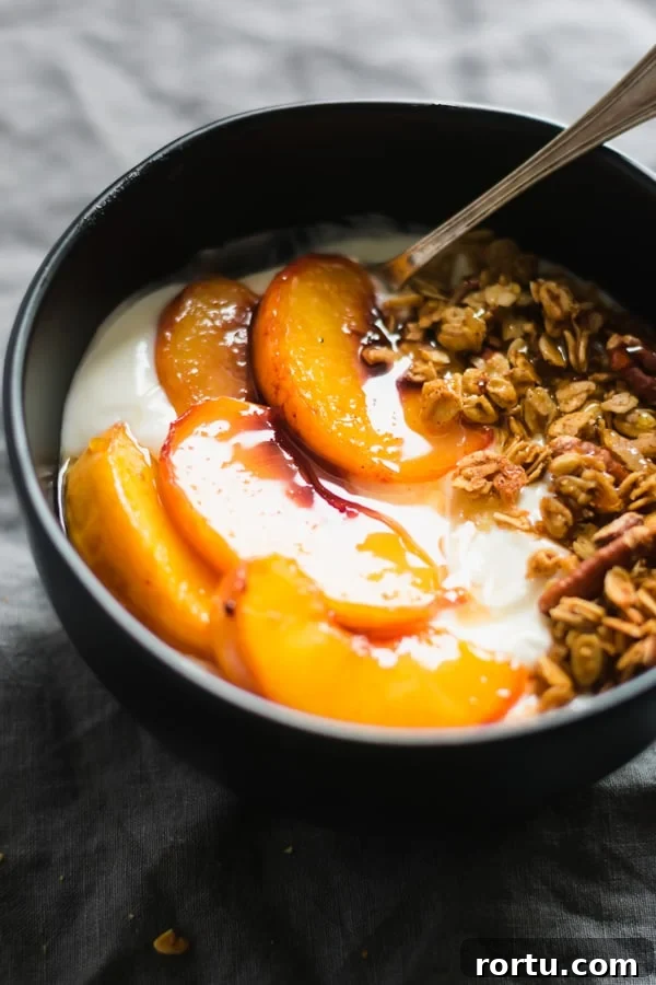 A bowl of greek yogurt with roasted peaches and maple granola.