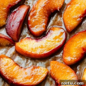A close-up of juicy roasted peach slices on a baking sheet.