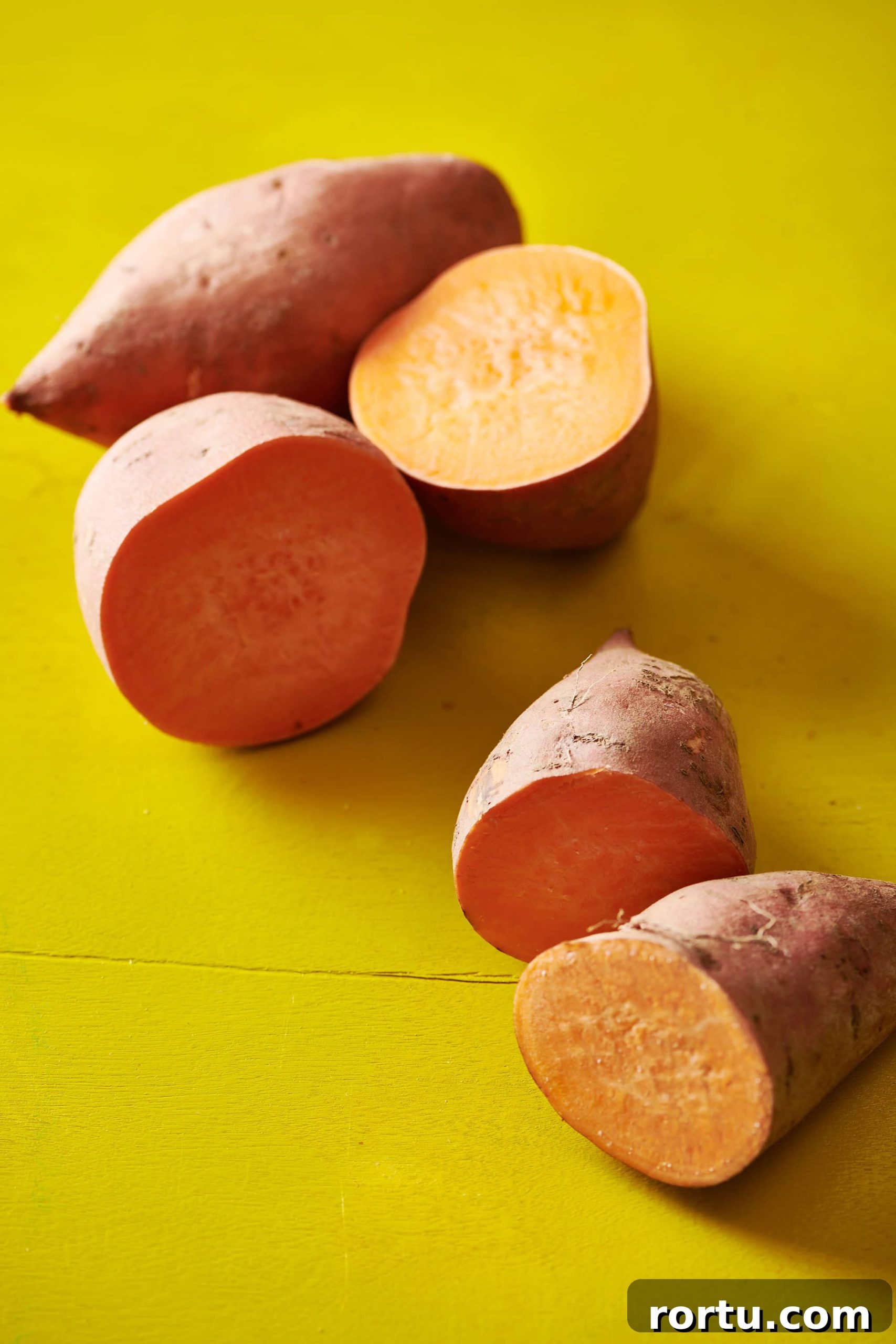 Halved sweet potatoes on a yellow table.