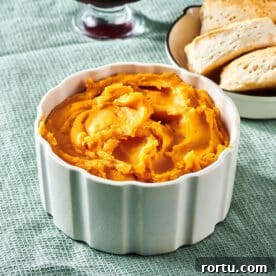 Mashed sweet potatoes in small bowl on table near biscuits.