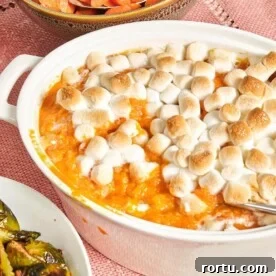 Baking dish of Sweet Potato Casserole with Marshmallows on a pink tablecloth.