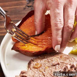 Woman using a fork to mash the inside of a baked sweet potato.