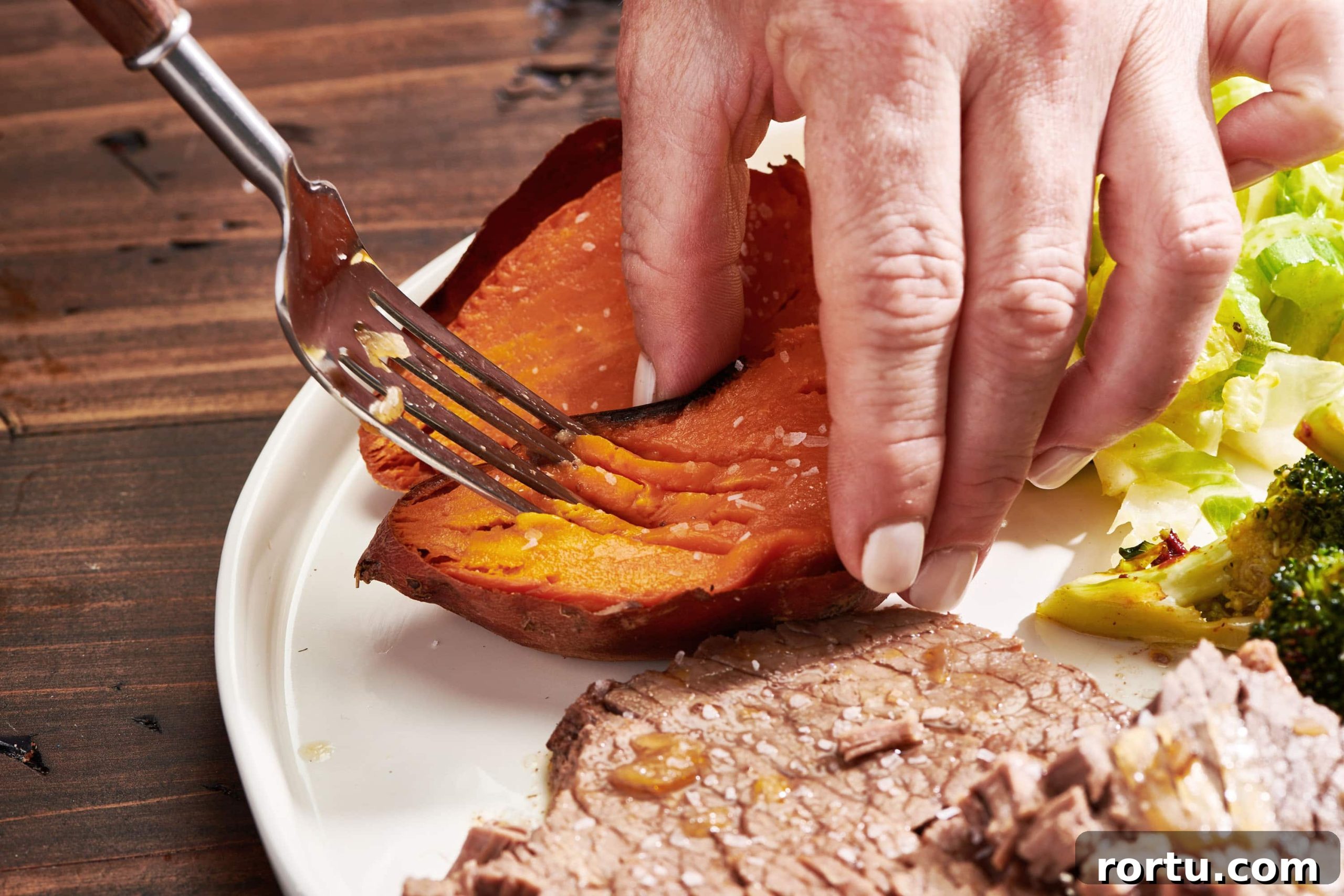 Woman using a fork to mash the inside of a baked sweet potato.