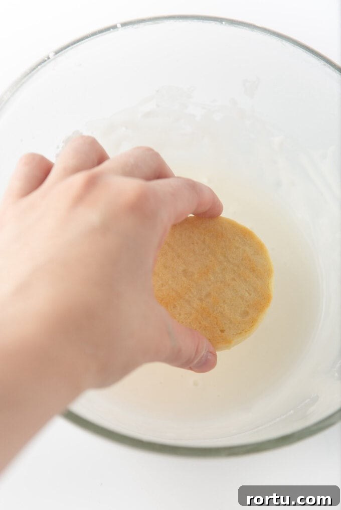 hand dipping top of sugar cookie into white icing