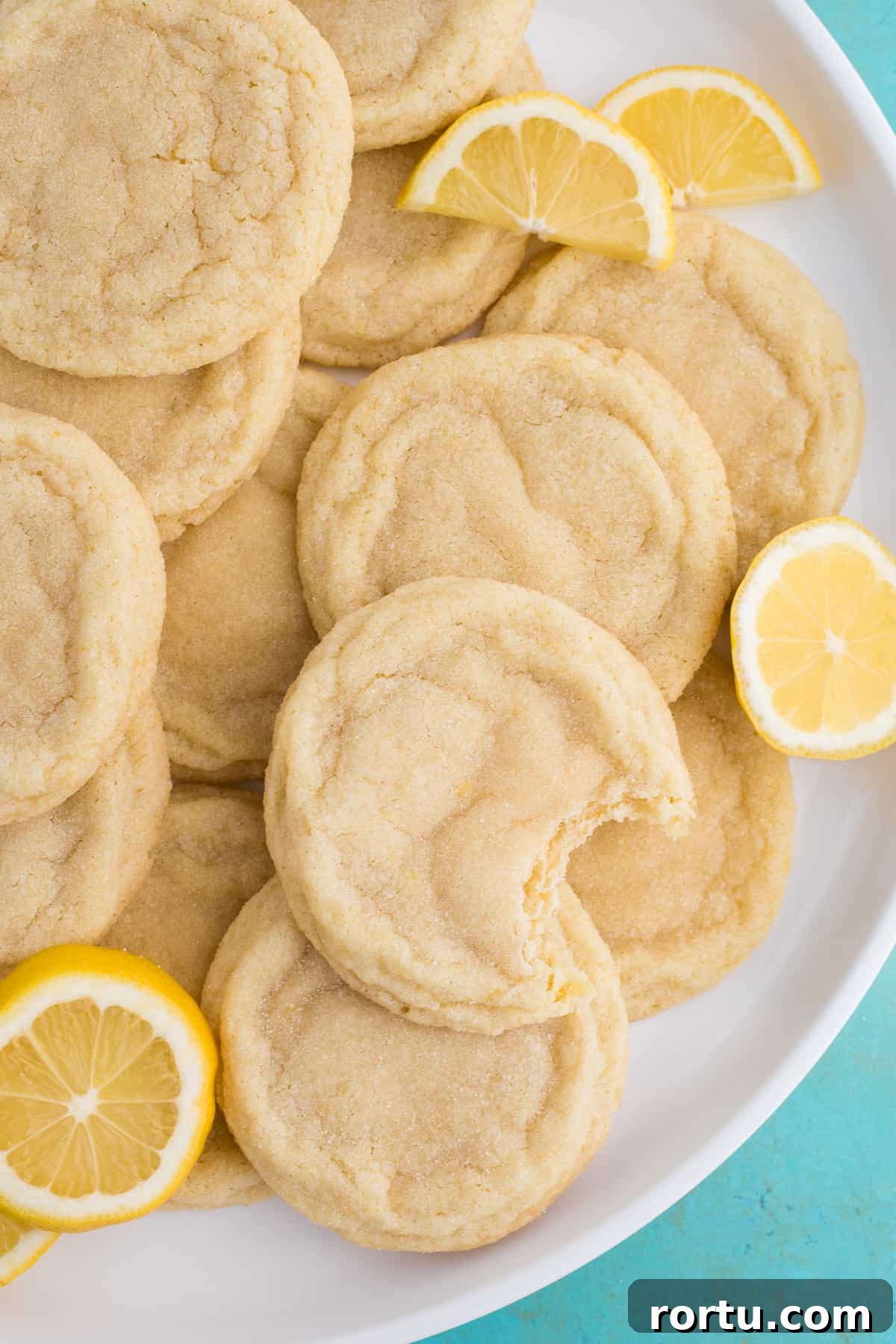 lemon sugar cookies with lemon slices on white plate on blue background