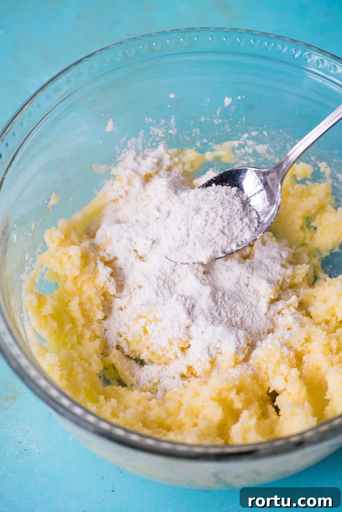 cookie batter with dry ingredients in a glass bowl on blue background