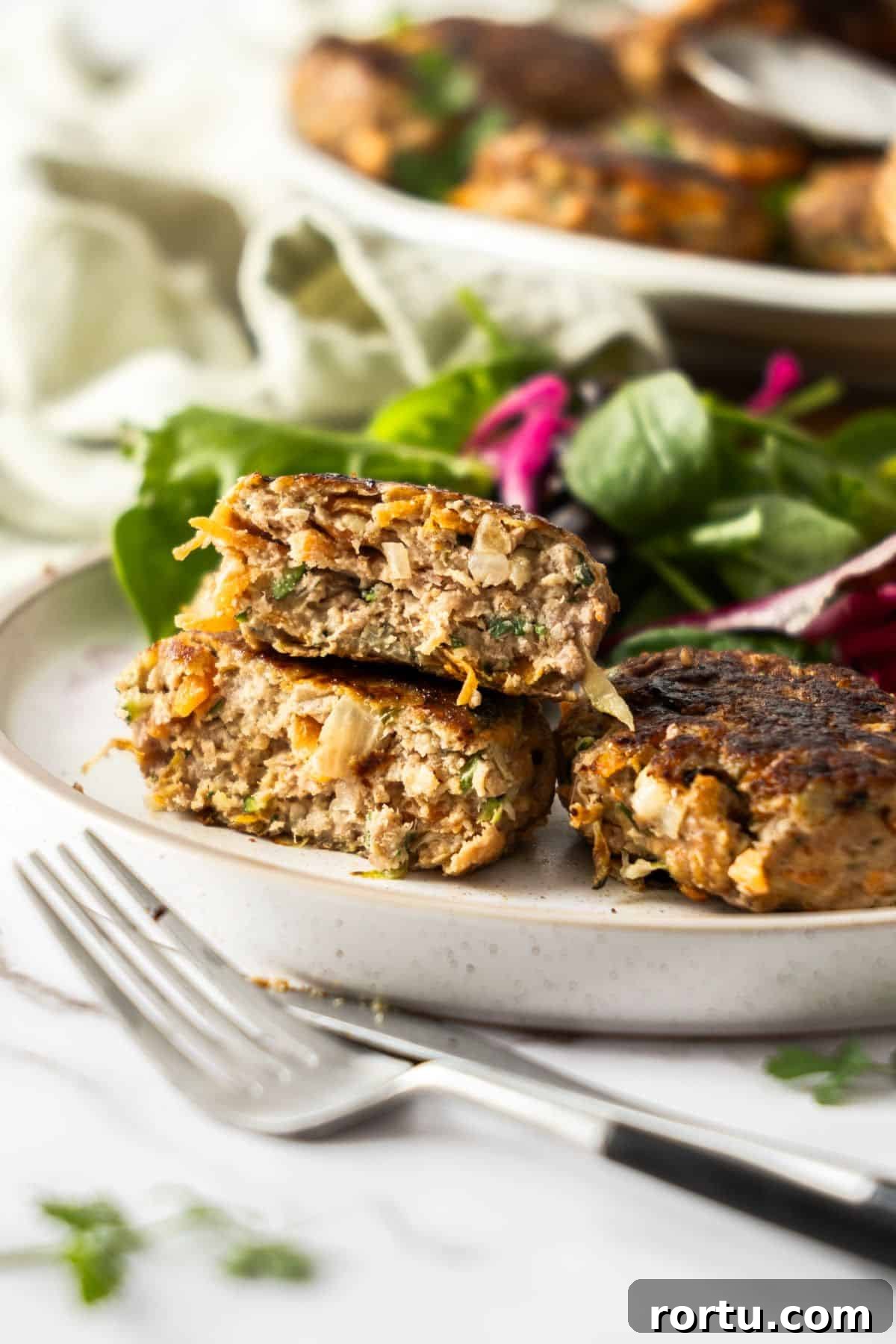 Round white plate with a serving of Turkey Patties, one cut in half to show the texture, and a salad on the side.