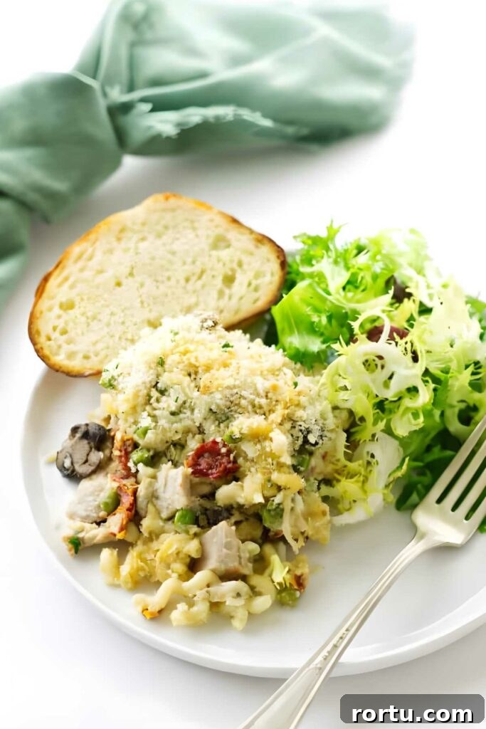 Creamy Turkey Tetrazzini Recipe for Leftovers and Holiday Meals 4 Turkey casserole with breadcrumbs, bread slice, and salad on a white plate.