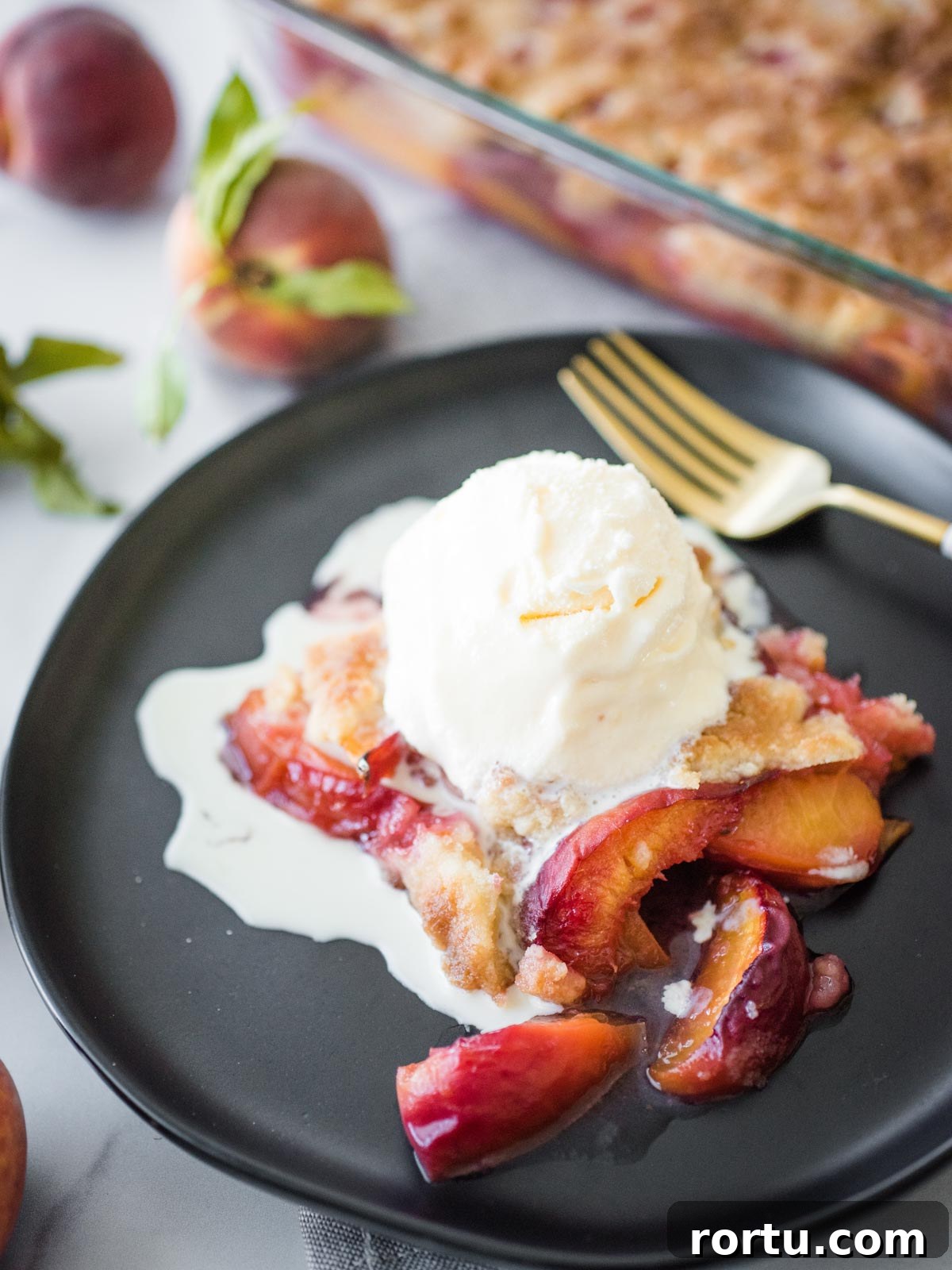peach cobbler on a black plate topped with ice cream