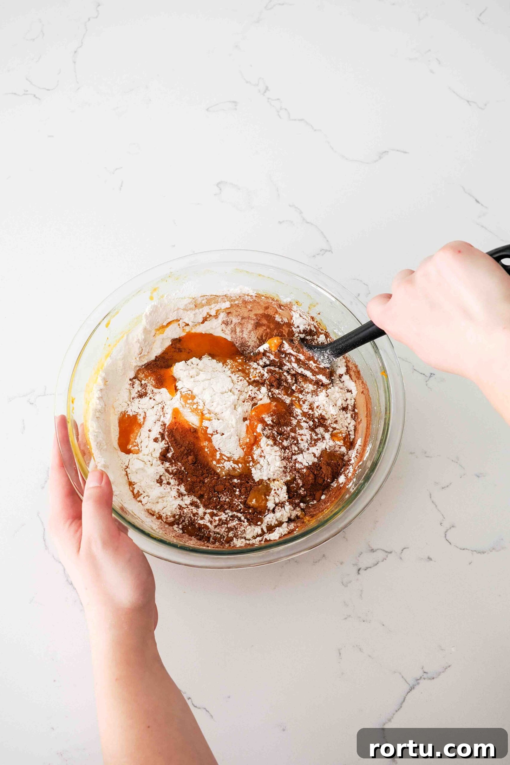 Chocolate Pumpkin Muffins Recipe — Moist Spiced Chocolate Muffins 6 Two hands use a spatula to stir in the dry ingredients into a wet pumpkin batter.