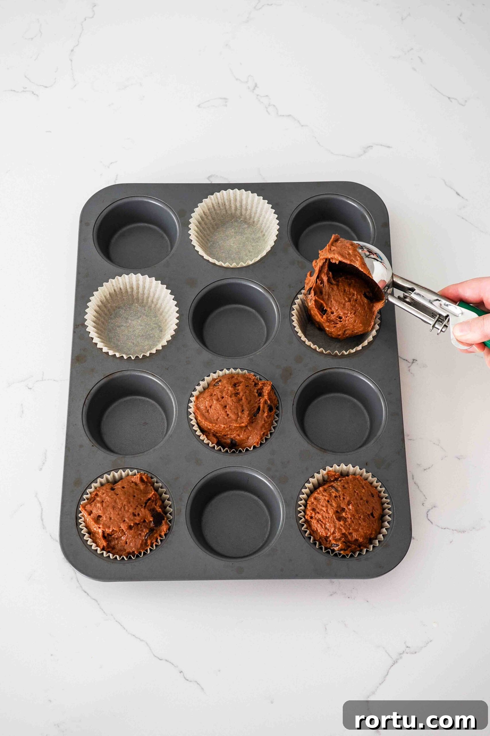 Chocolate Pumpkin Muffins Recipe — Moist Spiced Chocolate Muffins 8 A hand scoops chocolate pumpkin muffin batter into a lined muffin pan.