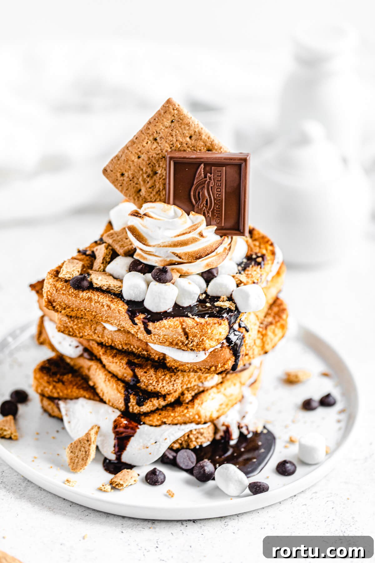 stack of French toast sandwiches topped with marshmallows, toasted meringue, chocolate chips, chocolate sauce and graham crackers on a white plate