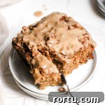 A square slice of apple coffee cake with maple glaze on a small white plate with a fork.