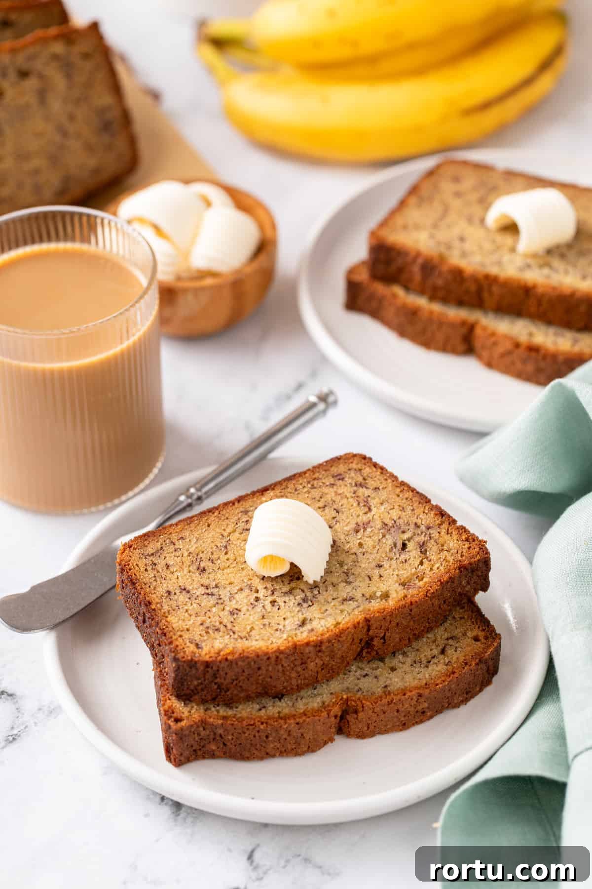 Two slices of dominique ansel's banana bread on a white plate, with a second plate of the bread in the background.
