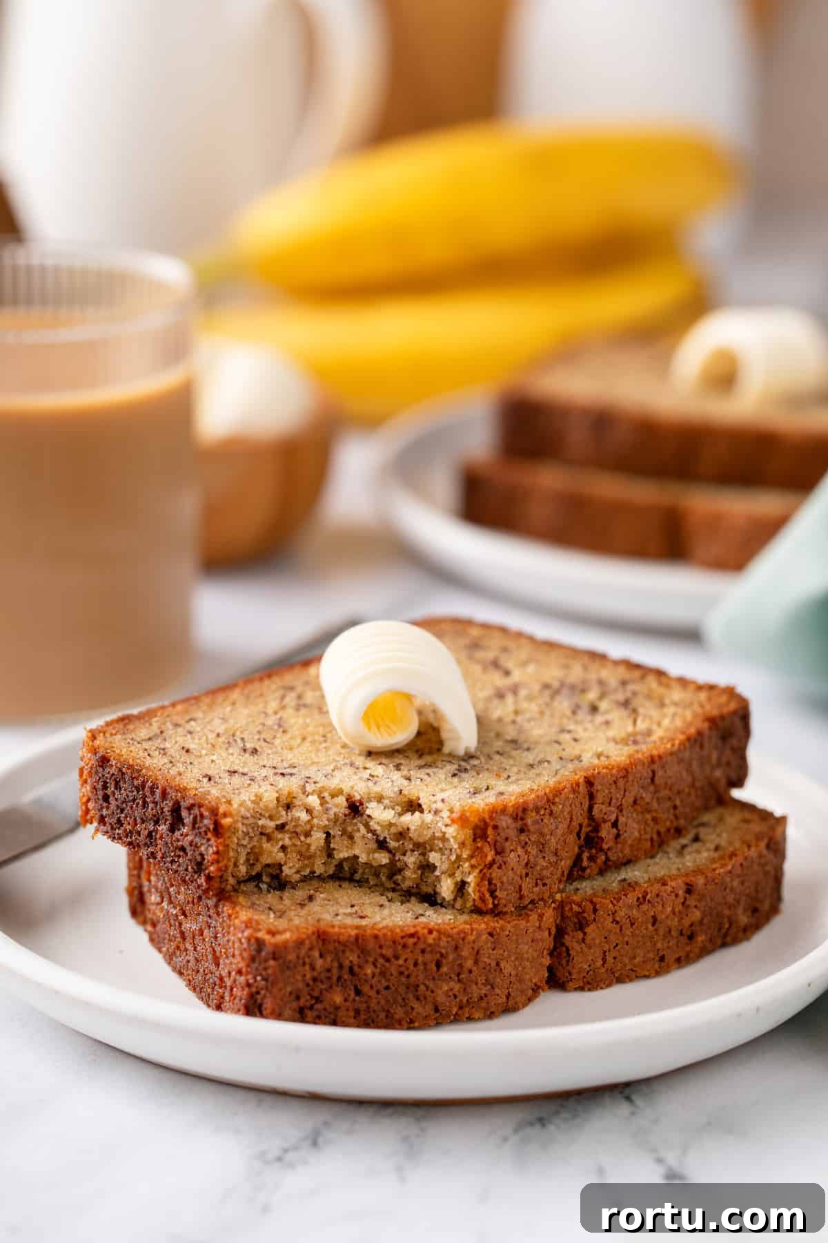 Two slices of banana bread stacked on a white plate. A bite has been taken from the corner of the top slice.