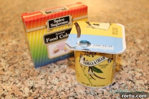 A box of food coloring and a single serving of vanilla yogurt on a counter