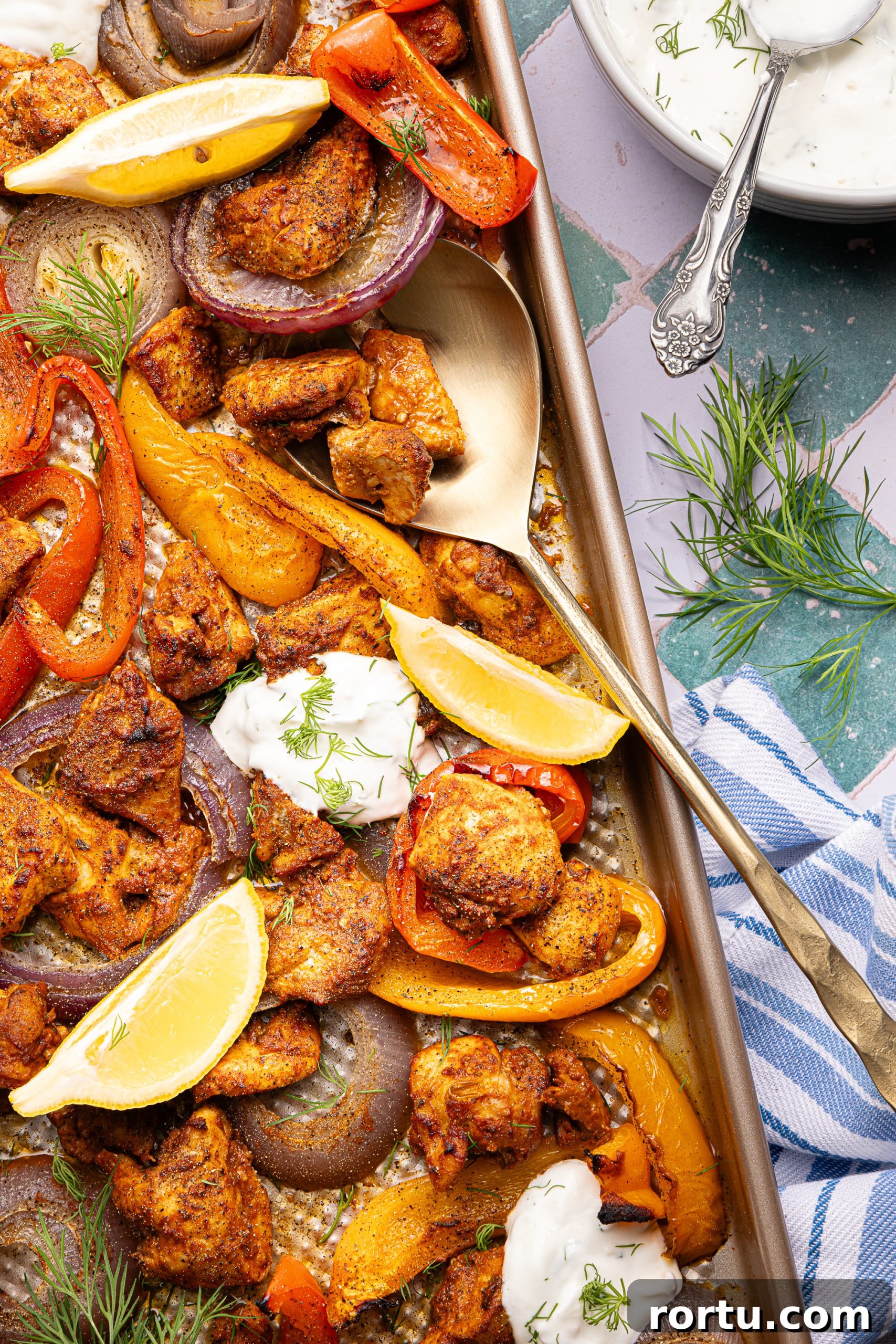 Mediterranean Sheet Pan Chicken with Lemon Garlic Yogurt Sauce 12 A metal spatula diggin into a Mediterranean chicken sheet pan dinner with dollops of lemon-garlic yogurt sauce