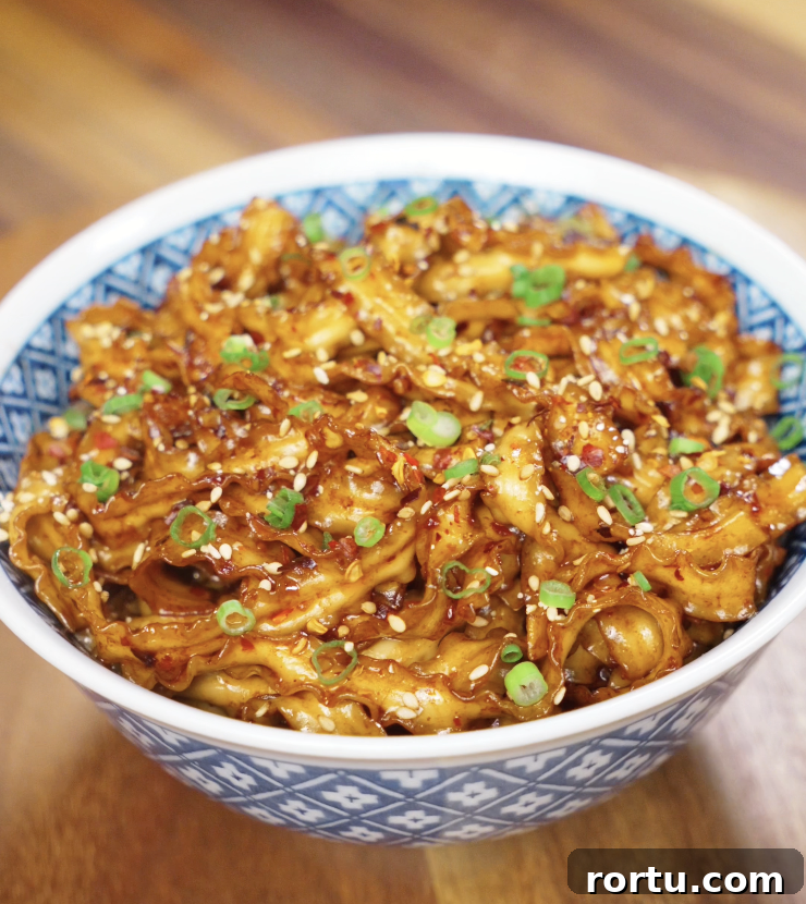 A serving of chili garlic butter noodles in a bowl, glistening with sauce and garnished with sesame seeds and scallions.