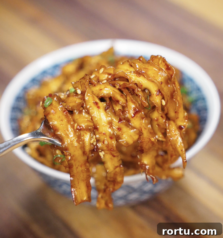 A chopstick lift of saucy noodles, showing the glistening strands coated in chili garlic butter.