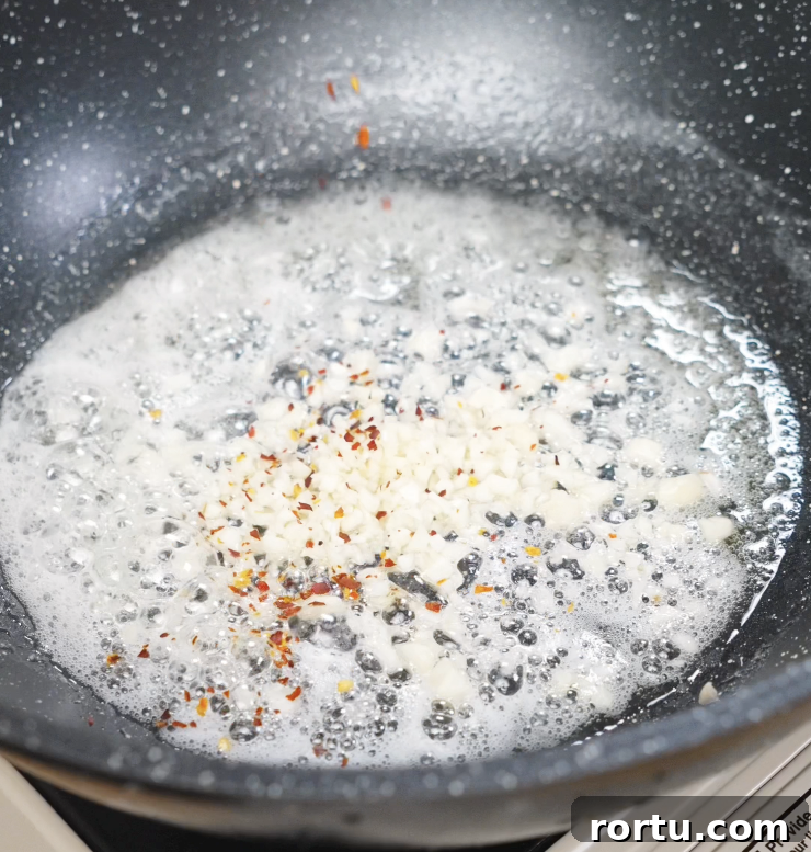 Minced garlic sizzling in melted butter with red chili flakes, releasing a fragrant aroma.