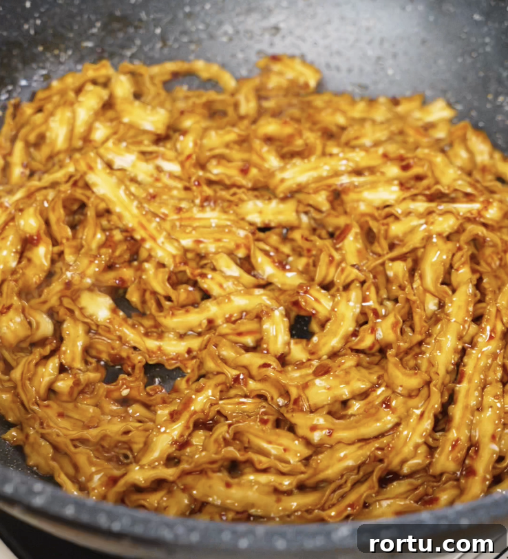 Cooked noodles being tossed into the pan, coated in the glossy, spicy chili garlic butter sauce.