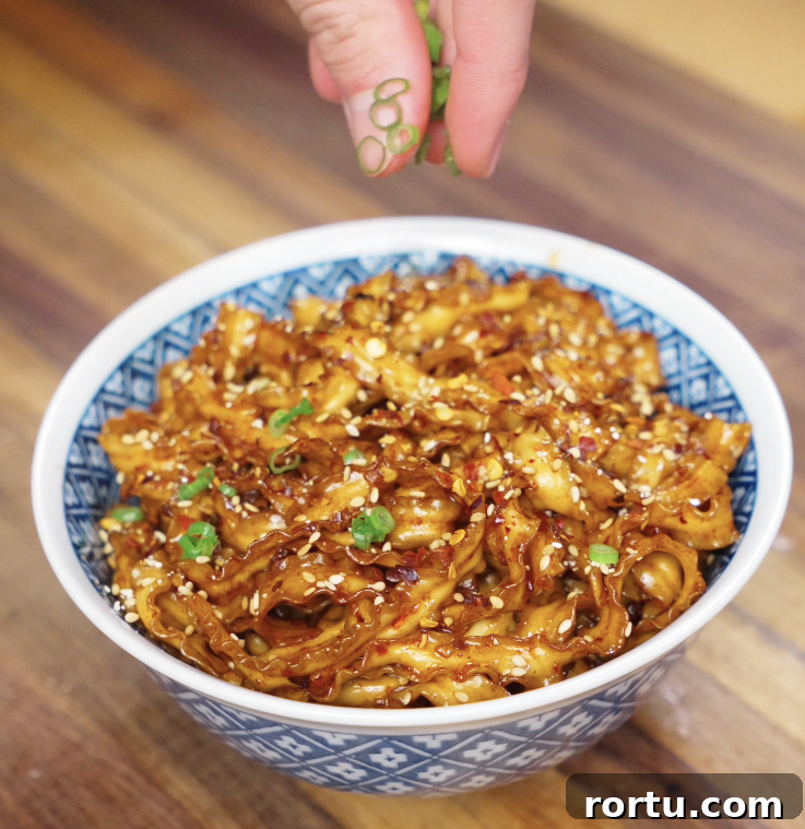 A neatly twirled bowl of noodles with garlic chili oil, scallions, and sesame seeds, ready to eat.
