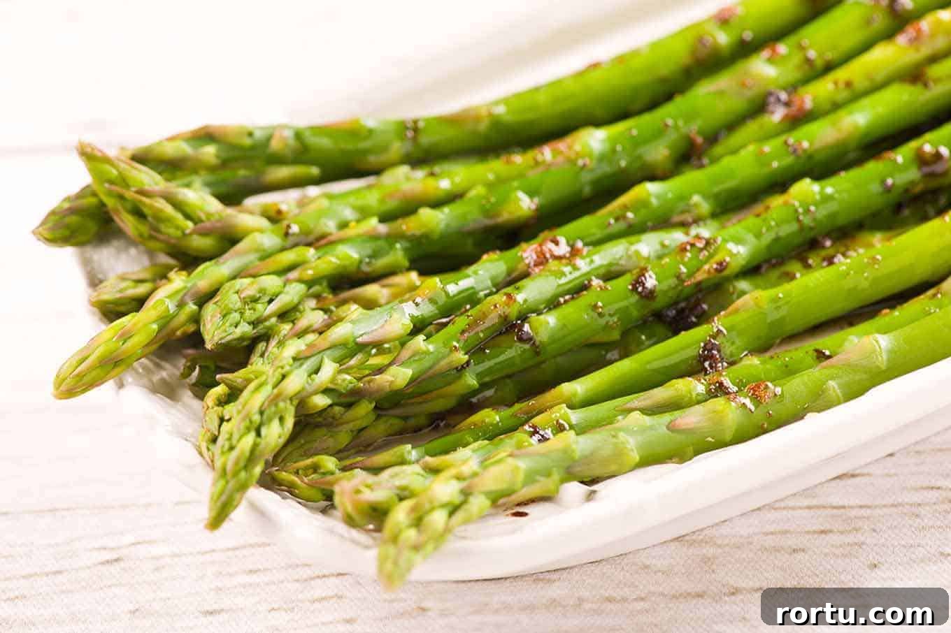 Steamed asparagus spears tossed in brown butter and balsamic vinegar on a white serving plate.