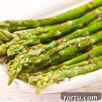 Steamed asparagus spears tossed in brown butter and balsamic vinegar on a white serving plate.
