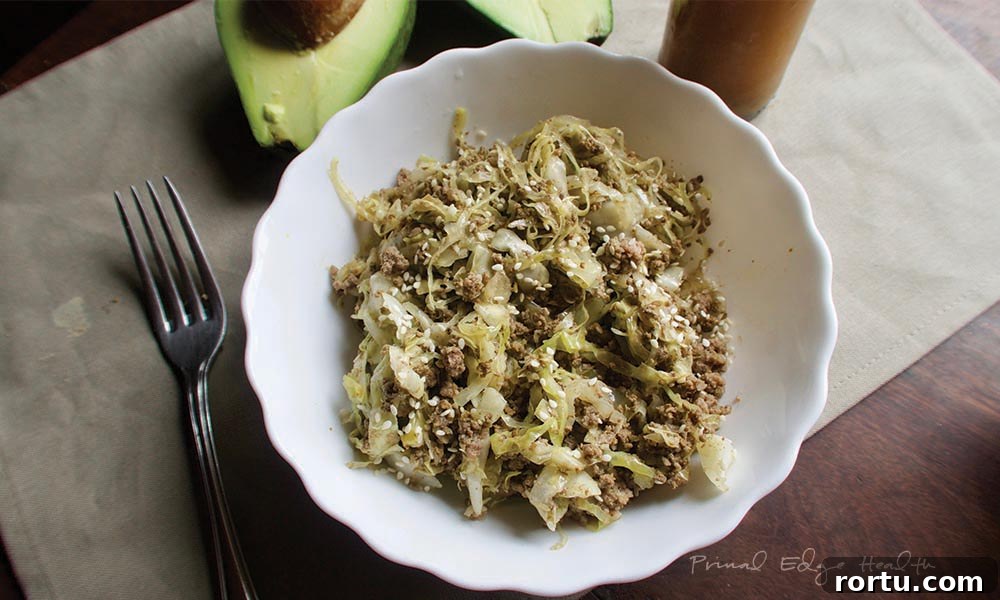 A serving of cabbage noodles with beef in a white bowl on a wooden surface.
