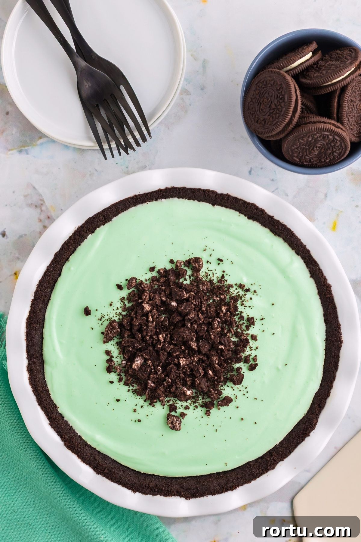 Creamy Mint Grasshopper Pie Recipe That Impresses 4 Grasshopper pie in a white pie dish with oreos on the table.