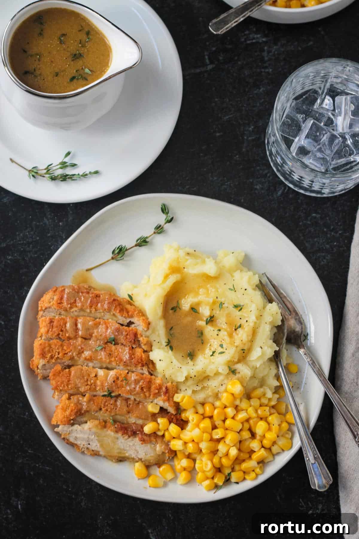 Dinner plate with sliced vegan chicken, corn, and mashed potatoes with gravy.
