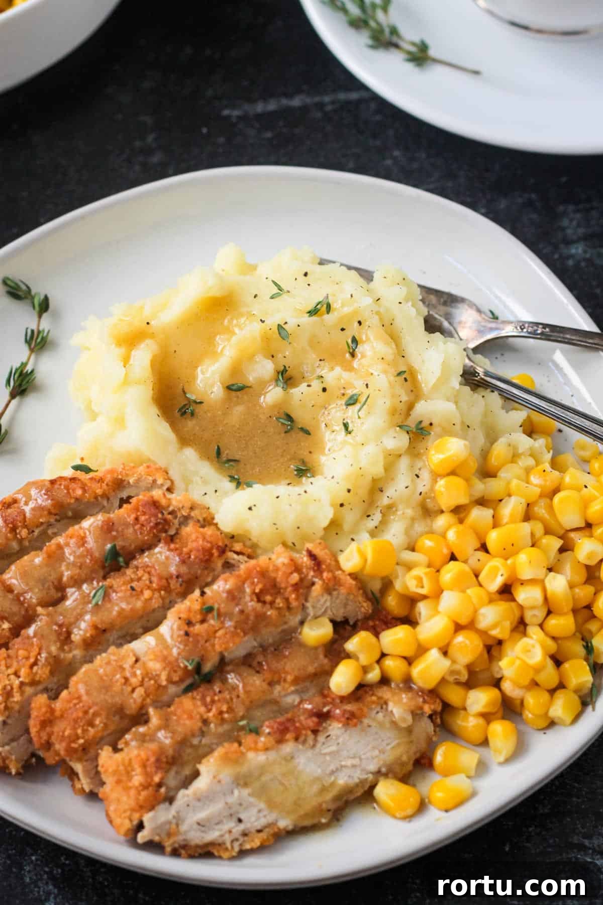 Close up of mashed potatoes topped with gravy on a plate with vegan chicken and corn.