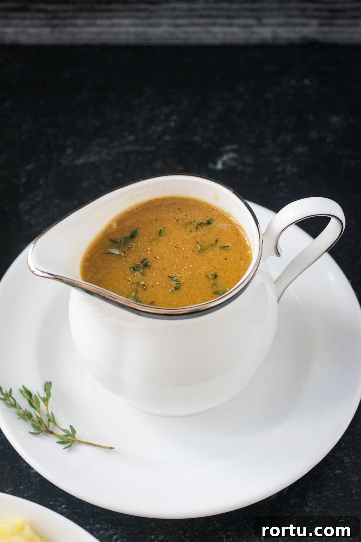 Small white pitcher of gravy garnished with fresh thyme leaves.