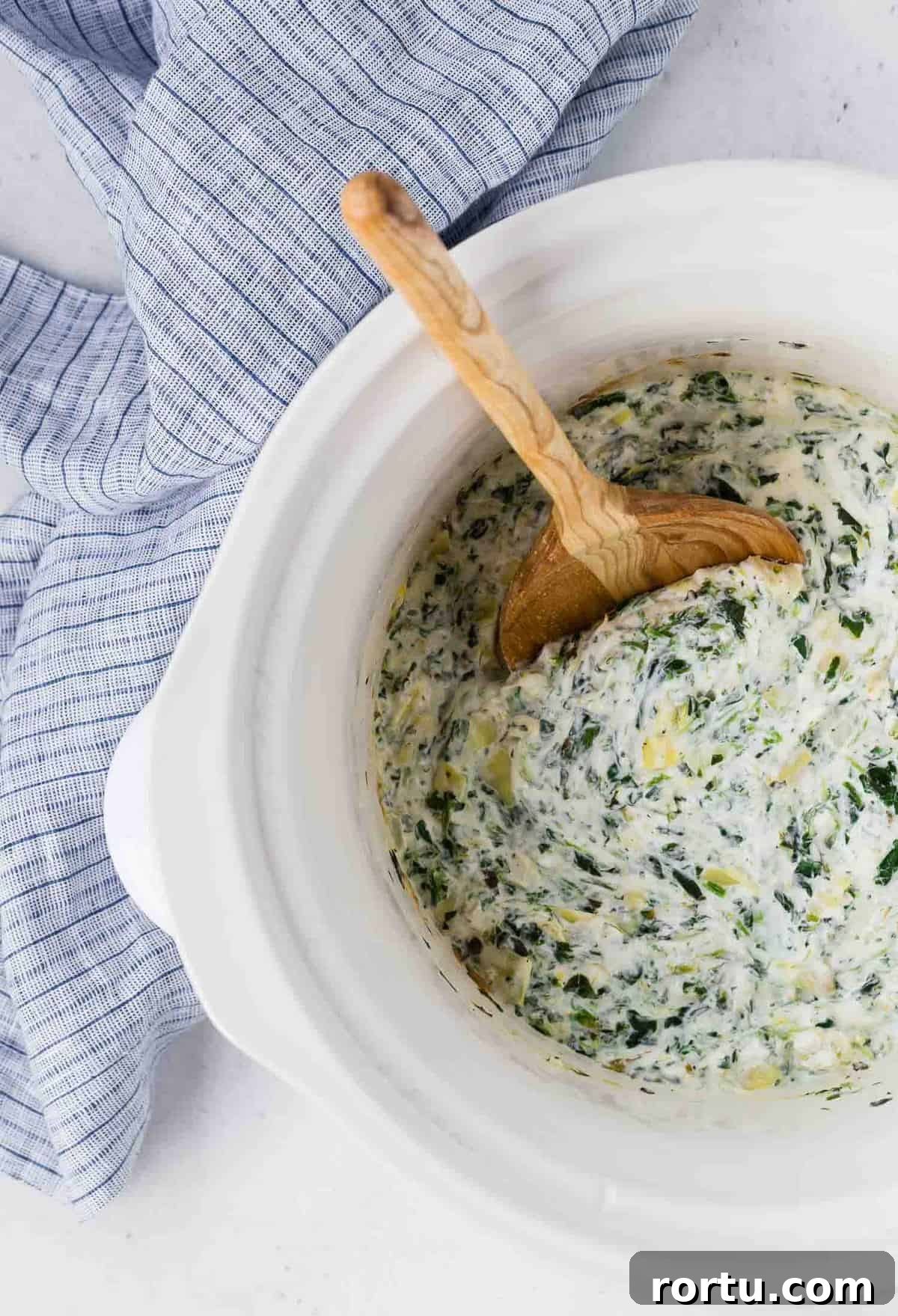 Overhead view of spinach artichoke dip in a white slow cooker.