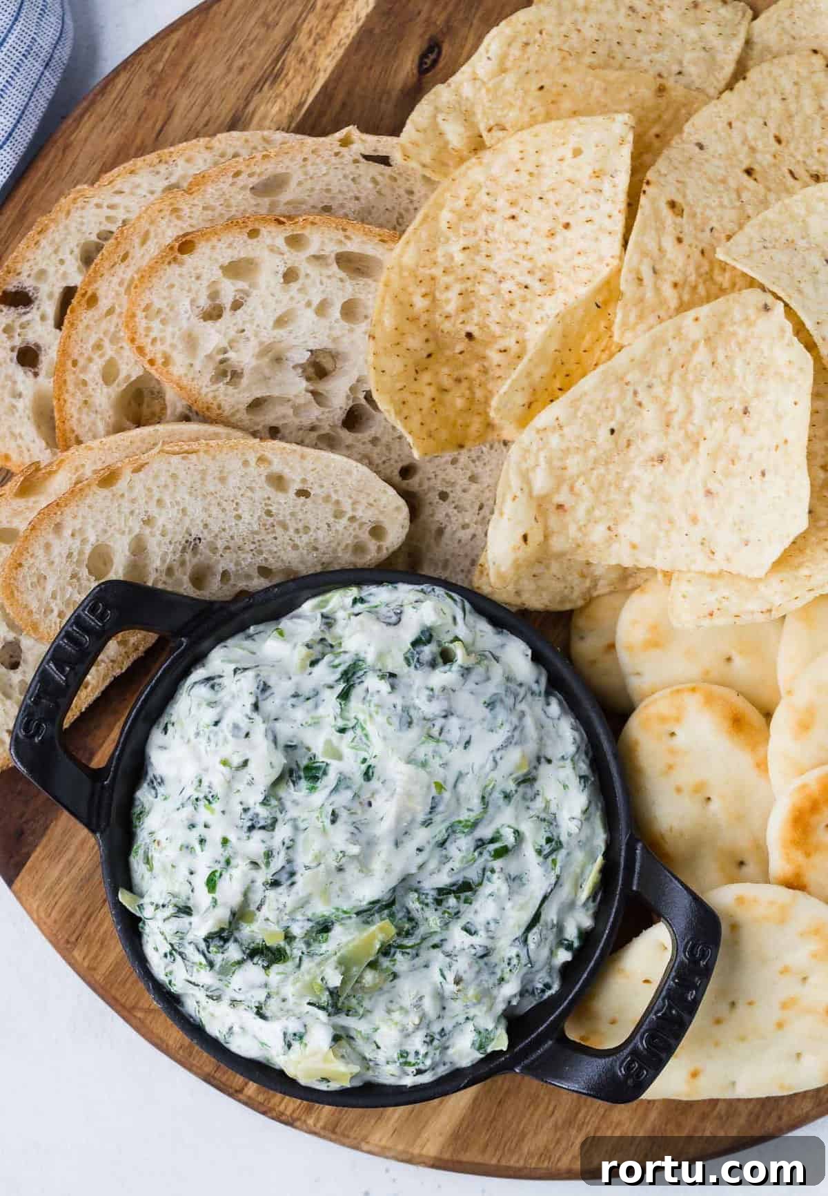 Overhead view of a small black dish of dip made with spinach and artichokes, surrounded by chips and bread.